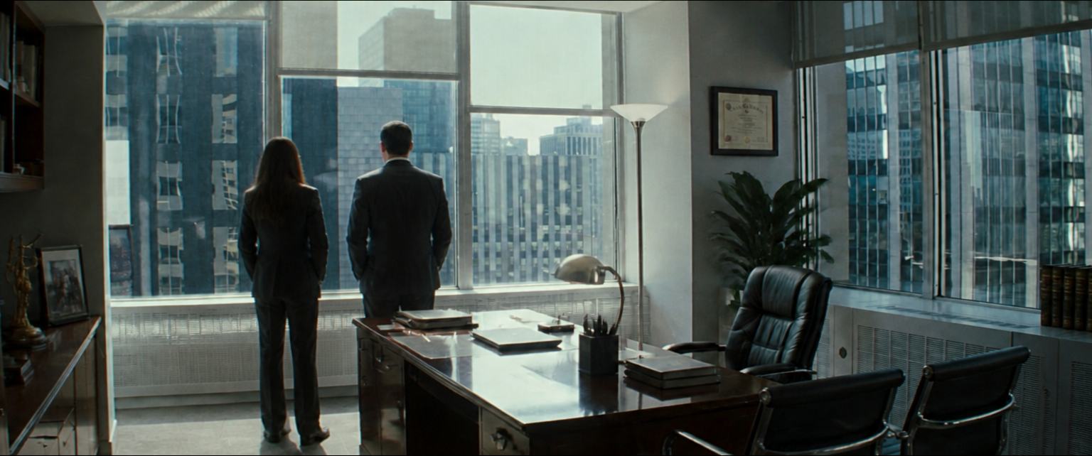 Two lawyers look out over the city from a corner office